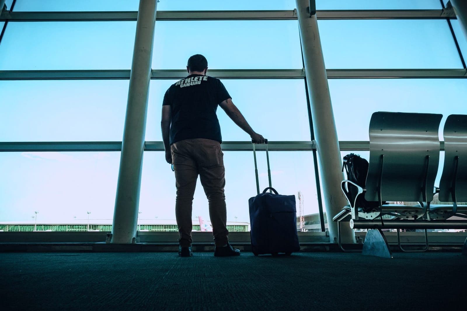 Traveler with a rolling suitcase silhouetted against an airport terminal window at dawn