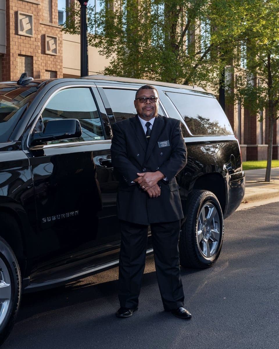 Professional chauffeur in a suit standing confidently beside a black luxury SUV