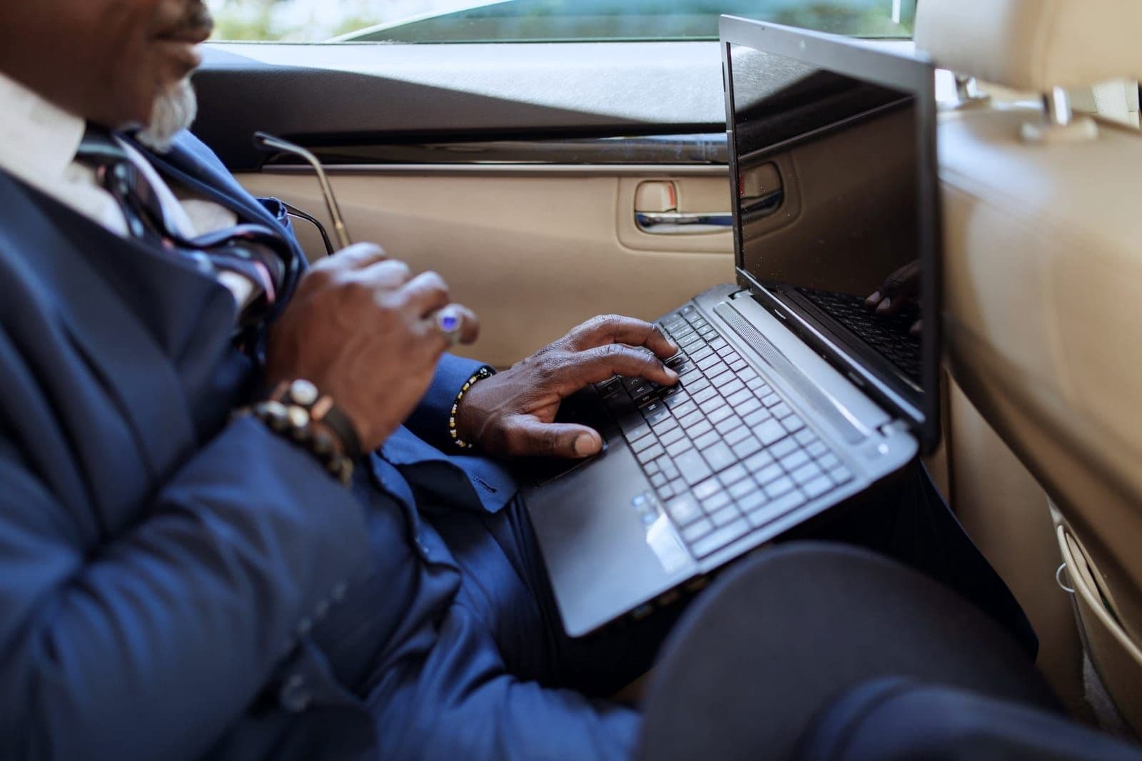 Businessperson typing on a laptop in the rear seat of a car, face angled out of frame