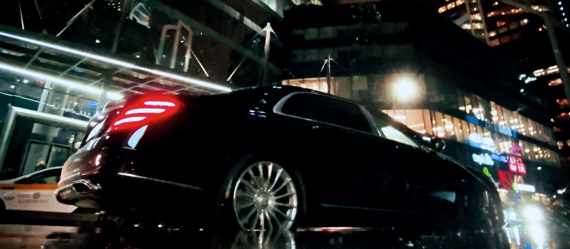 Black chauffeur sedan on a wet Manhattan street at night, city lights reflecting off the pavement