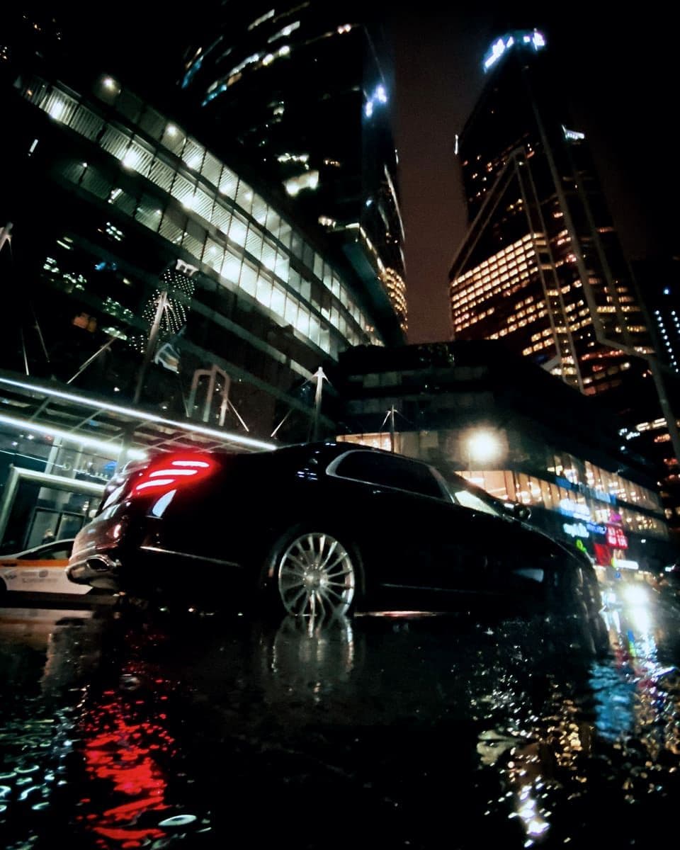 Black chauffeur sedan on a wet Manhattan street at night, city lights reflecting off the pavement