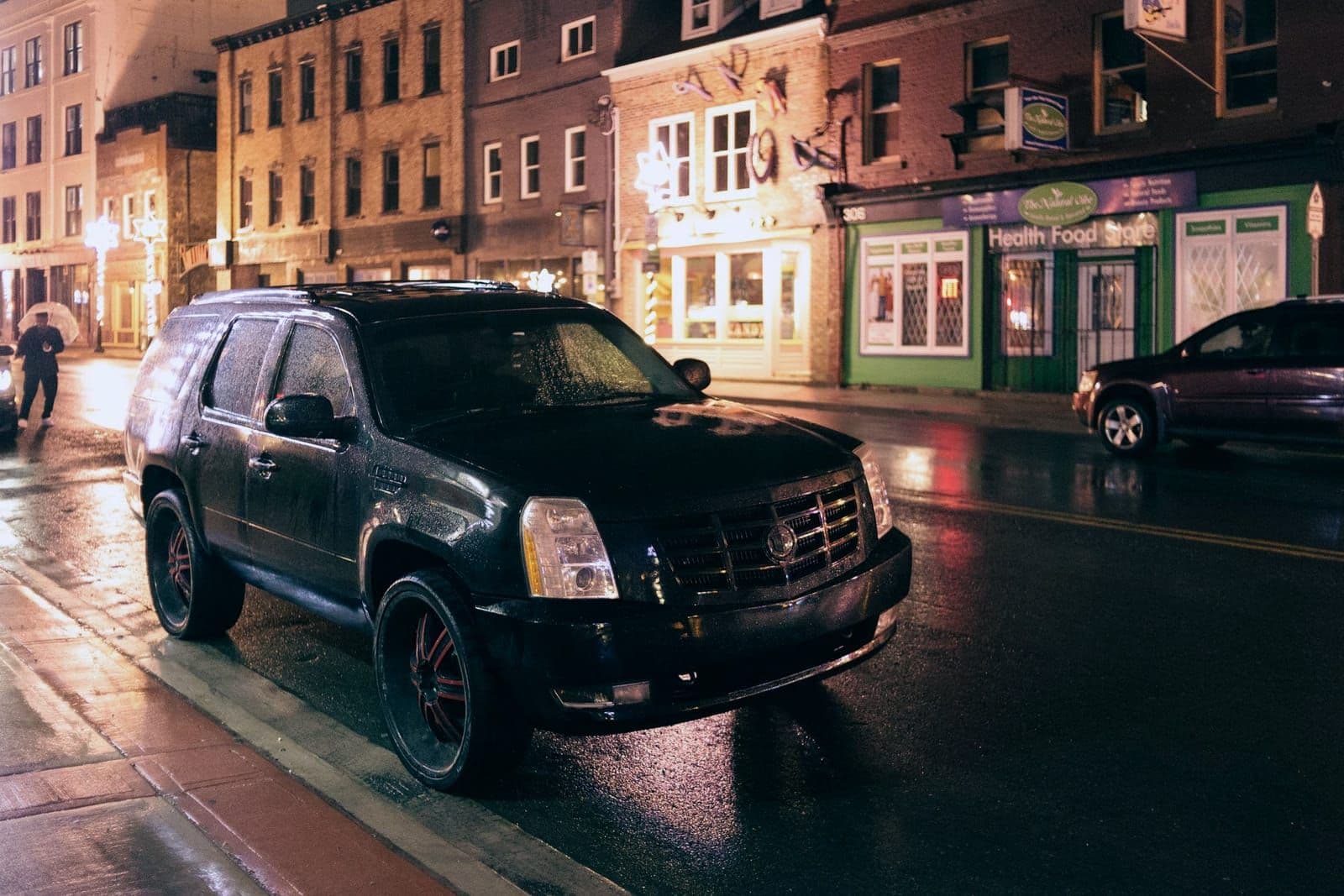 Black full-size luxury SUV parked on a city street at night, wet pavement